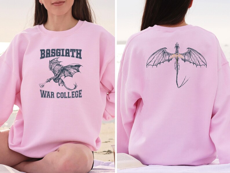 May include: Pink sweatshirt with a dragon graphic and the text "Basgiath War College" on the front. The back of the sweatshirt features a dragon graphic.