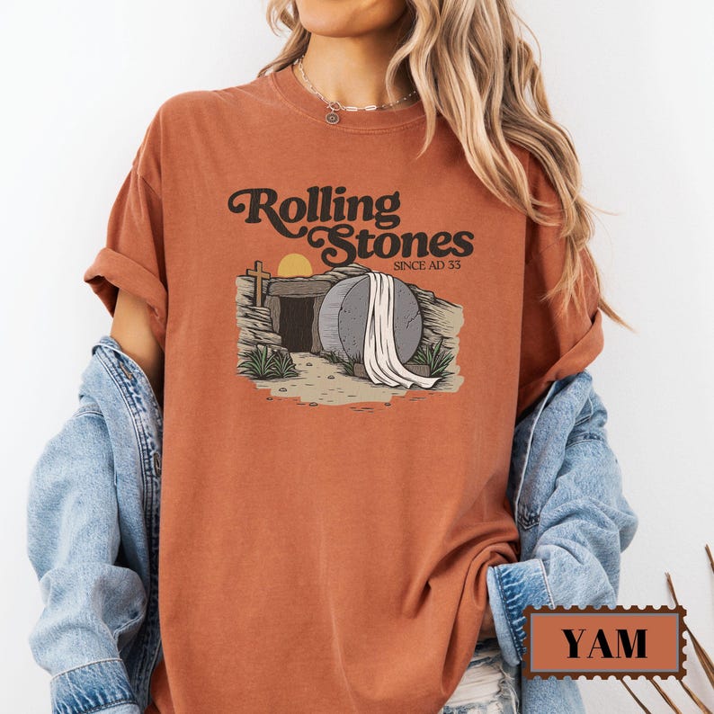 May include: A rust-colored t-shirt with a graphic of a stone tomb with a white sheet draped over it. The text "Rolling Stones Since AD 33" is above the tomb.