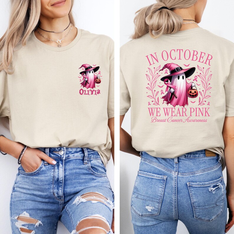 May include: A light beige t-shirt with a pink ghost wearing a witch hat and holding a pumpkin. The text "In October We Wear Pink" and "Breast Cancer Awareness" is on the back of the shirt. The front of the shirt has the text "Olivia" and a smaller pink ghost.