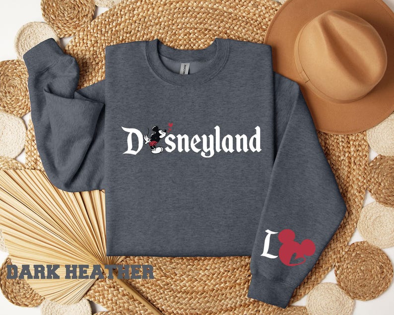 Puede incluir: Sudadera gris oscuro con la palabra "Disneyland" en escritura blanca, con Mickey Mouse. La manga izquierda tiene una cabeza de Mickey Mouse roja y la letra "L".