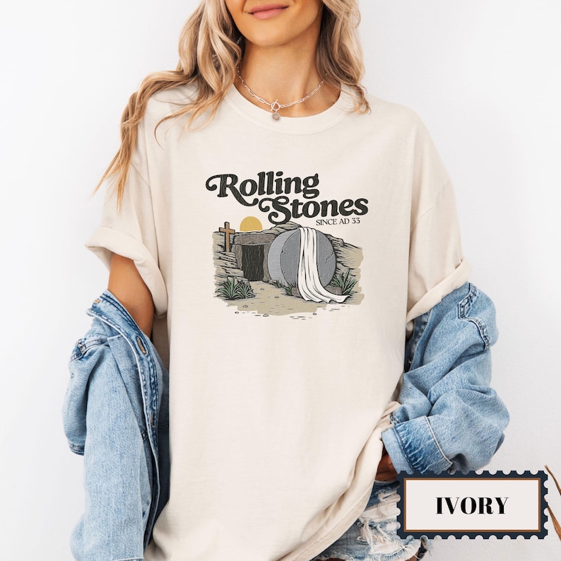 May include: A beige t-shirt with a graphic of a tomb with a white sheet and the text "Rolling Stones Since AD 33". The shirt is labeled "Ivory".