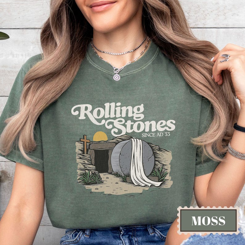 May include: A green t-shirt with a vintage-style graphic of a stone tomb with a white sheet draped over it. The text "Rolling Stones Since AD 33" is printed on the shirt.