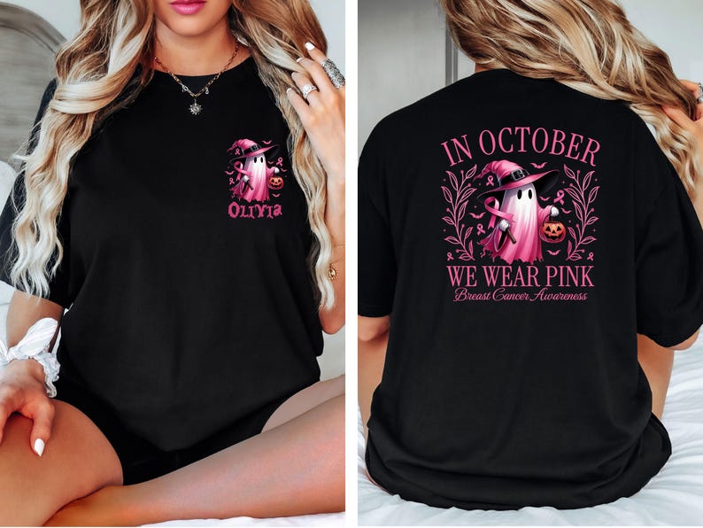 May include: Black t-shirt with a pink ghost wearing a witch hat and holding a pumpkin. The text "In October We Wear Pink" and "Breast Cancer Awareness" is printed on the back. The front of the shirt has a pink ghost with a witch hat and the name "Olivia" printed below.