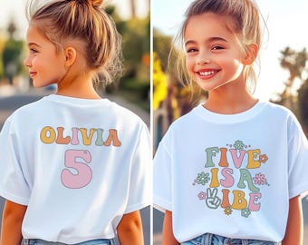 Puede incluir: Camisetas blancas con texto y gráficos coloridos. Una camiseta tiene el nombre "Olivia" y el número "5" en la espalda. La otra camiseta dice "Five is a Vibe" con flores y un signo de la paz. Ambas camisetas son usadas por una persona joven.