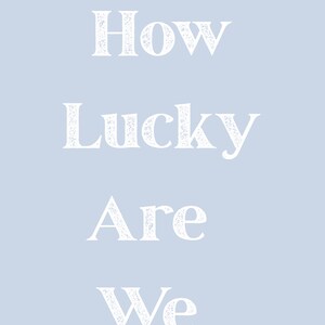 May include: A light blue background with the white text "How Lucky Are We" in a distressed font. The text is vertically centered, creating a simple and elegant design.
