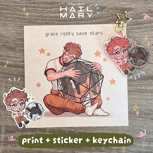 Op de afbeelding: Een Project Hail Mary merchandise set bestaande uit een vierkante art print, een gestanste sticker en een acryl sleutelhanger. De illustratie toont een personage met bruin haar en een bril die een zwarte geometrische vorm omhelst.