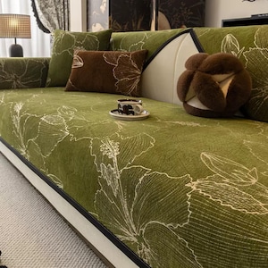May include: A green sofa with white floral patterns and matching throw pillows. The sofa has a dark trim and is accessorized with a brown pillow and a decorative fur ball. A cup and saucer sit on the sofa.