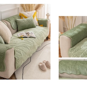 May include: A light green sofa cover set with a leaf pattern. The set includes a sofa cover, armrest covers, and decorative cushions. The cushions are in shades of green and cream. A book and a yellow flower are on the sofa.