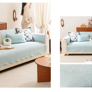 Puede incluir: Una funda de sofá azul claro con borde festoneado y un intrincado diseño floral en relieve. El sofá se combina con cojines a juego de varios tamaños y patrones. El conjunto está en un salón luminoso.