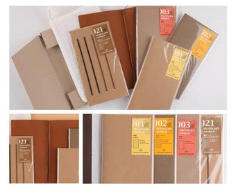 Puede incluir: Un conjunto de seis recargas para Traveler's Notebook en varios colores, incluyendo marrón, beige y negro. Cada recarga tiene un número diferente y el texto "Traveler's Notebook" impreso en ella.