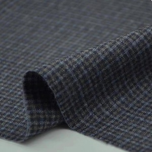 May include: A close-up shot of a dark grey fabric with a small houndstooth pattern. The fabric is folded, showing its texture and colour variations, including hints of blue and brown.