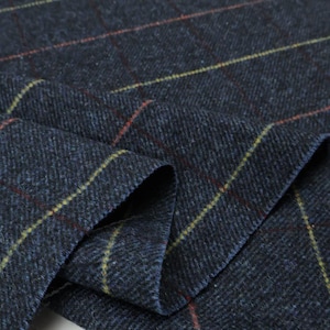 Puede incluir: Primer plano de una tela azul marino con un patrón de cuadros. La tela tiene líneas amarillas y rojas que se cruzan para crear un diseño de cuadrícula. La tela está doblada, mostrando textura y profundidad.