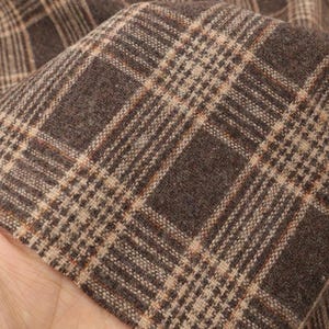 Può includere: Primo piano di un tessuto a quadri marrone e beige. Il tessuto ha un aspetto strutturato con un classico motivo a quadri. I colori caldi e neutri sono adatti a vari progetti di cucito e artigianato.