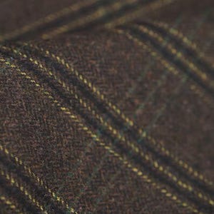 May include: Close-up of a brown tweed fabric with yellow and green stripes. The fabric has a textured appearance and a diagonal pattern. The tweed material is likely used for clothing or upholstery.