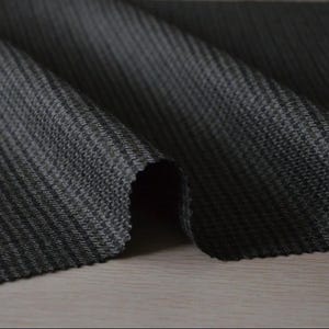 May include: Close-up of a dark gray fabric with a subtle, textured pattern. The fabric is folded, revealing its weave and depth. The material appears to be a medium-weight textile, suitable for various apparel or home decor projects.