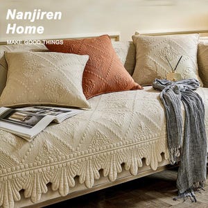 May include: Beige sofa with decorative pillows in shades of beige and rust. The pillows have textured patterns. A gray scarf and an open magazine rest on the sofa. The text "Nanjiren Home" and "MAKE GOOD THINGS" are visible.