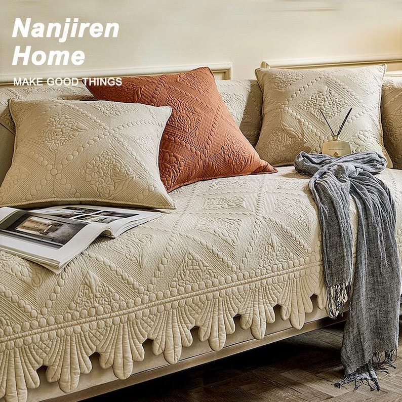 May include: Beige sofa with decorative pillows in shades of beige and rust. The pillows have textured patterns. A gray scarf and an open magazine rest on the sofa. The text "Nanjiren Home" and "MAKE GOOD THINGS" are visible.