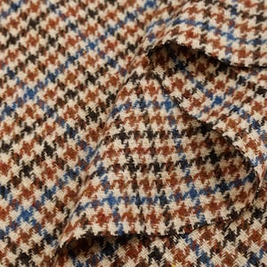 Könnte beinhalten: Nahaufnahme eines gefalteten Stoffes mit einem klassischen Hahnentrittmuster. Der Stoff weist ein sich wiederholendes Design aus kleinen Karos in Braun, Schwarz, Blau und Creme auf. Die Textur wirkt weich und gewebt, geeignet für Kleidung oder Polster.