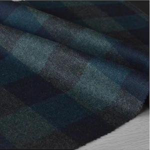 May include: Close-up of a folded fabric with a plaid pattern. The fabric features a blend of dark teal, navy, and charcoal gray colors. The texture appears soft and slightly textured, with visible woven threads. The overall aesthetic is classic and suitable for apparel or home decor.