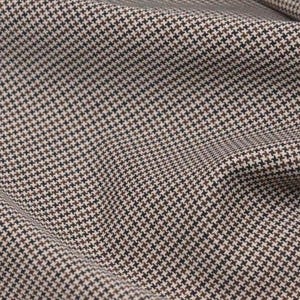 May include: Close-up of a fabric with a classic houndstooth pattern. The fabric features a repeating pattern of small, four-pointed shapes in brown, black, and off-white, creating a textured appearance. The fabric is likely used for clothing or upholstery.
