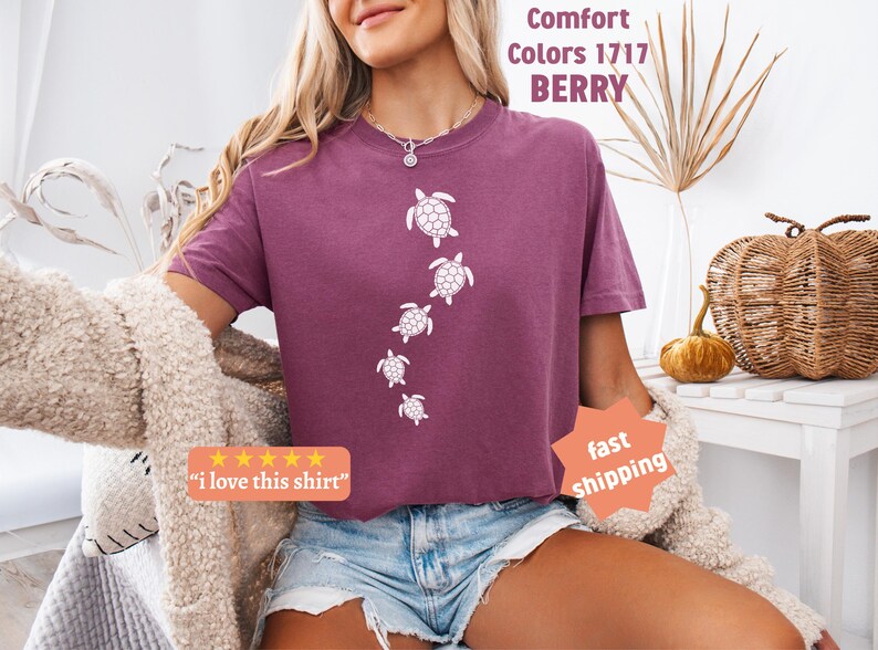 May include: Berry-colored t-shirt with a crew neck featuring a white turtle design. The shirt has the text "Comfort Colors 1717 BERRY" and a five-star review sticker that says "I love this shirt".