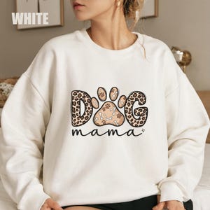 May include: White sweatshirt with the text "DOG mama" in a playful design. The word "DOG" is in a leopard print pattern, and the paw print is filled with bones. A comfortable, casual top for dog lovers.