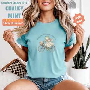May include: A turquoise t-shirt with the text "Comfort Colors 1717 CHALKY MINT" and "i love this shirt". The shirt features a frog on a bicycle with the text "off to cause a Kerfuffle at mahjong".