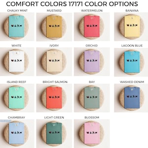 May include: A grid of t-shirts in various colors, including mint, mustard, and watermelon. Each shirt features a graphic design and is displayed on a woven mat. The text "COMFORT COLORS 17171 COLOR OPTIONS" is at the top.