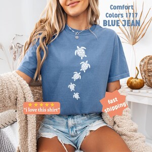 May include: Blue jean-colored t-shirt with a white turtle design. The shirt has the text "Comfort Colors 1717 BLUE JEAN" printed on it. The shirt also has the text "I love this shirt" printed on it.
