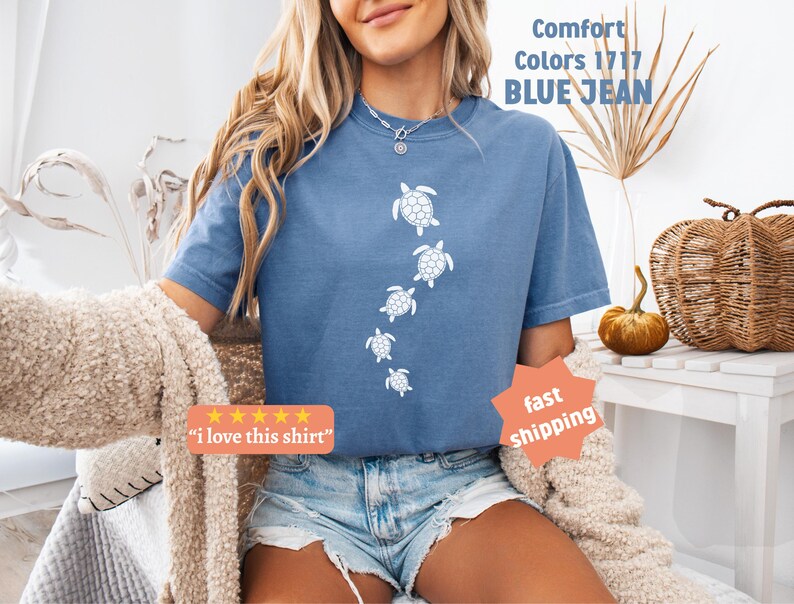 May include: Blue jean-colored t-shirt with a white turtle design. The shirt has the text "Comfort Colors 1717 BLUE JEAN" printed on it. The shirt also has the text "I love this shirt" printed on it.