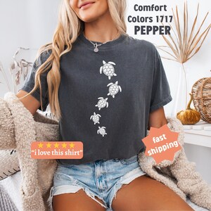 May include: Dark gray Comfort Colors t-shirt with a design of white turtles swimming downward. The shirt has the text "Comfort Colors 1717 PEPPER" and a sticker that says "I love this shirt".