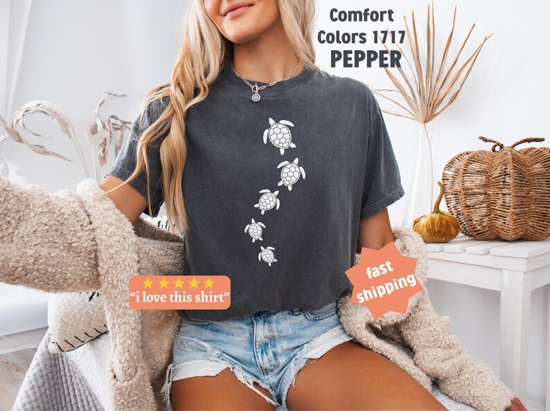 May include: Dark gray Comfort Colors t-shirt with a design of white turtles swimming downward. The shirt has the text "Comfort Colors 1717 PEPPER" and a sticker that says "I love this shirt".