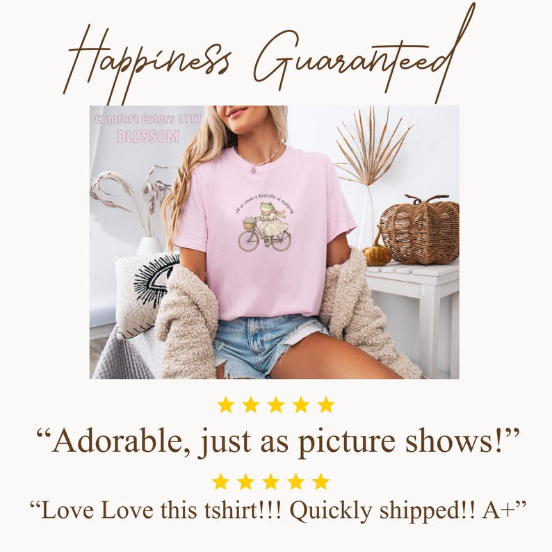 May include: A pale pink t-shirt featuring a frog on a bicycle graphic, with text above. The shirt is labelled "Comfort Colors 1717 BLOSSOM". The text "Happiness Guaranteed" is above the shirt. The shirt is worn with denim shorts.