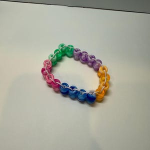 May include: A colorful bracelet made of round, translucent beads in a rainbow of colors: pink, green, blue, purple, and yellow. The beads are strung together on a white cord, creating a vibrant accessory.