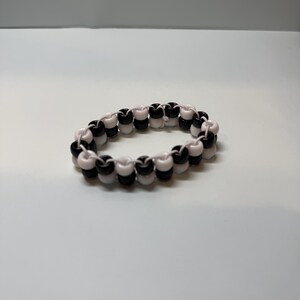 May include: A beaded bracelet featuring alternating black and white beads. The bracelet is made of small, round beads strung together to form a circular shape. The beads are evenly spaced, creating a symmetrical pattern. The bracelet is a simple, yet stylish accessory.