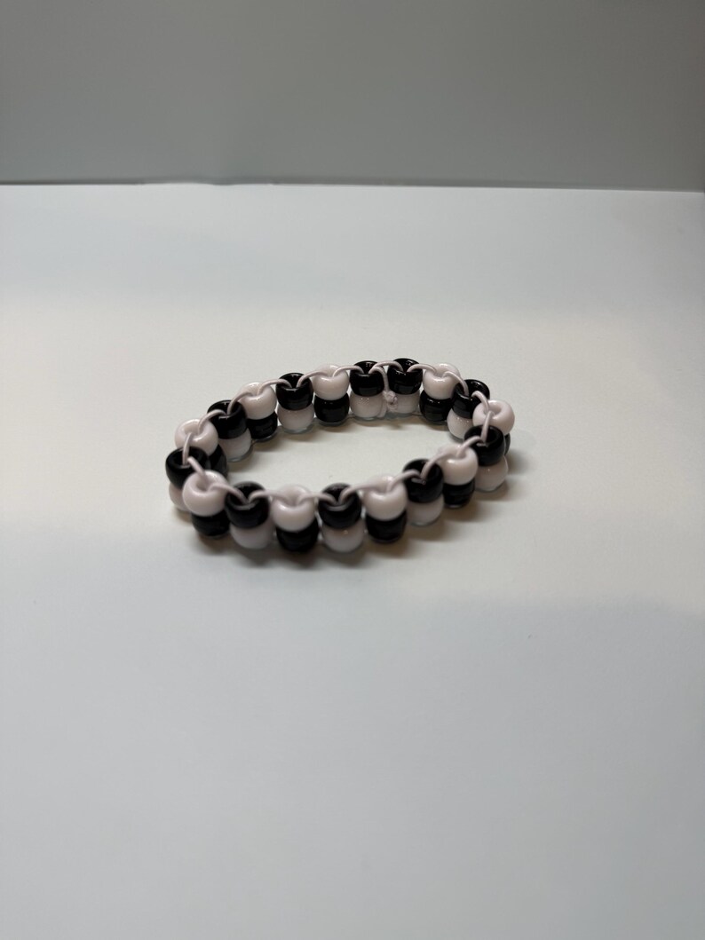 May include: A beaded bracelet featuring alternating black and white beads. The bracelet is made of small, round beads strung together to form a circular shape. The beads are evenly spaced, creating a symmetrical pattern. The bracelet is a simple, yet stylish accessory.