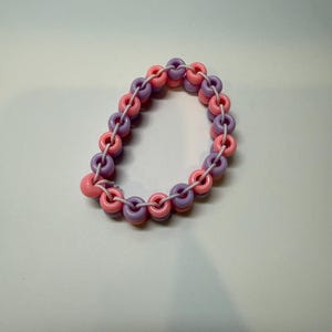 May include: A handmade bracelet featuring alternating pink and purple ring-shaped beads strung on a white cord. The bracelet has a playful, colorful design, perfect for adding a pop of color to any outfit. The beads are made of plastic.