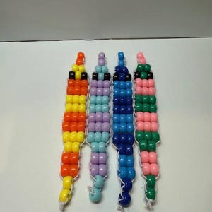May include: Four beaded bracelets in vibrant colors: orange, yellow, purple, blue, pink, and green. Each bracelet is strung on white cord, with a loop at the end. The bracelets are a fun and colorful accessory.