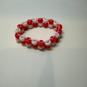May include: A handmade bracelet featuring alternating red and white beads strung on a white cord. The beaded accessory is designed in a circular shape, suitable for wrist wear. The bracelet is a vibrant accessory.