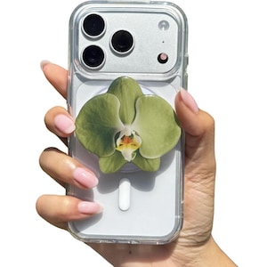 May include: A clear phone case with a green orchid flower design. The phone case has a clear back and a silver camera module. The orchid flower is a light green color with a white and yellow center.