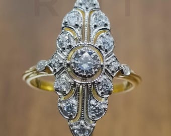 May include: A gold ring with a large, ornate, diamond-studded centerpiece. The centerpiece has a central, large, round diamond surrounded by smaller diamonds in a symmetrical, elongated design. The ring's band is gold.