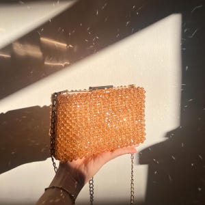 May include: A gold chain purse with a beaded body. The beads are a light brown color and create a shimmering effect.