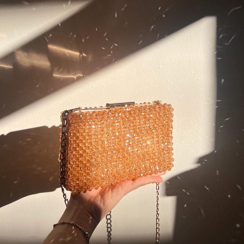May include: A gold chain purse with a beaded body. The beads are a light brown color and create a shimmering effect.