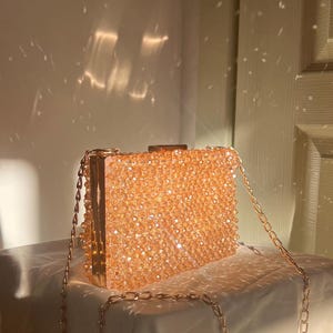 May include: A gold chain purse with a clear body covered in small, sparkly, peach-colored beads.