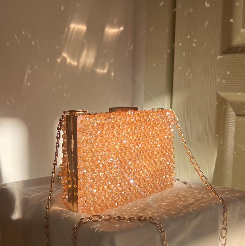 May include: A gold chain purse with a clear body covered in small, sparkly, peach-colored beads.