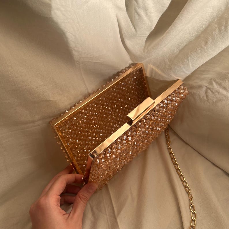May include: A gold clutch purse with a beaded exterior. The purse has a clasp closure and a chain strap.