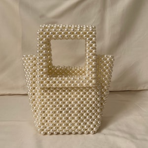 Op de afbeelding: Een klein, wit, geperst handtasje met een vierkante vorm en een bovenste handvat.