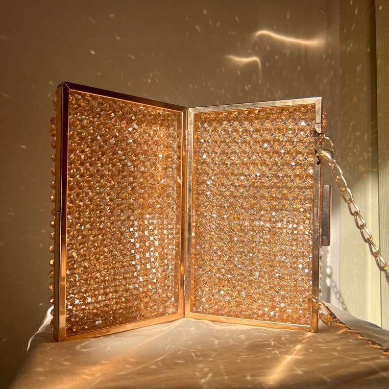 May include: A gold-toned, hinged clutch purse with a beaded exterior and a chain strap. The purse is open, revealing the beaded interior.