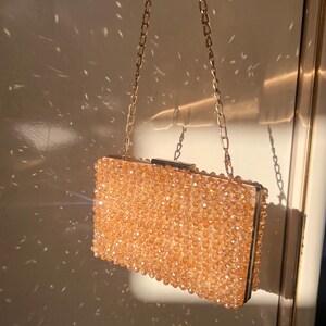 May include: A gold chain purse with a beaded clutch. The clutch is made of small, round, light brown beads.