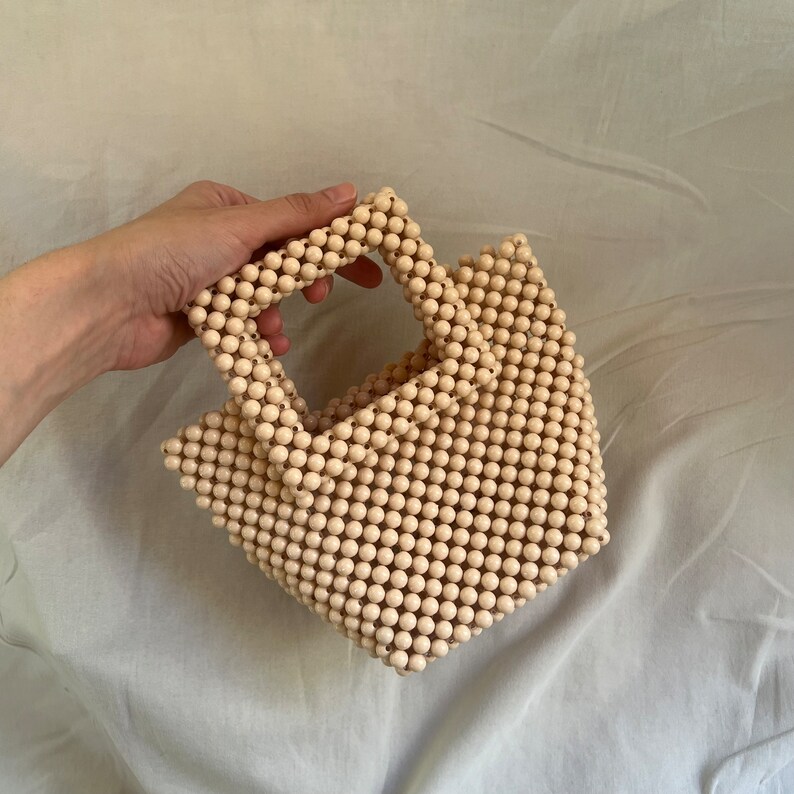 May include: A small, cream-colored beaded bag with a square top handle. The bag is made entirely of small, round beads.